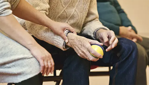 The Birches at Villa Rica - Old man holding a ball assited by caregiver